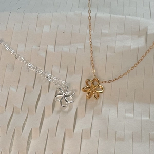 Detailed close-up of hollow flower pendants in silver and gold on fine cable chains