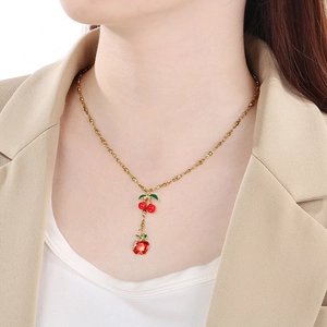 Close-up of a gold necklace featuring red cherry and rhinestone apple pendants on a model