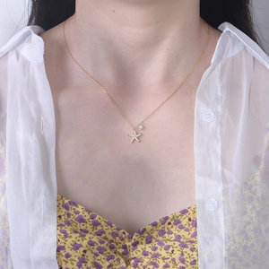 Detailed view of a gold starfish necklace with small diamonds and pearl on a model