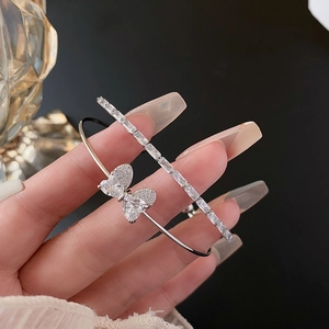 Detail of silver bow bangle and rectangular zircon bracelet set held in hand