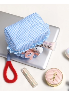 Blue checkered quilted makeup bag with ruffle trim and red handle on a laptop