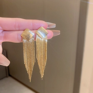 Detail view of long gold tassel earrings with square brushed metal studs and snake chains