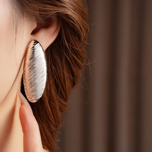 Close-up of a silver-toned oval earring with horizontal textured design on model's ear