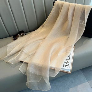 Close-up of beige silk scarf with subtle shimmer texture draped on a leather sofa