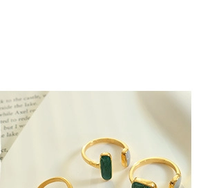 Detailed shot of three gold adjustable rings with green and grey stones on a white tray