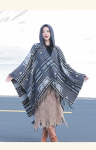 Detail of grey hooded knit poncho shawl featuring geometric patterns and fringe trim