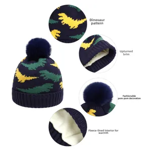 Detail view of navy baby knit hat with dinosaur pattern, pompom, and warm fleece lining