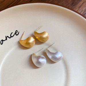 Detailed view of matte gold and silver teardrop earrings on a ceramic display