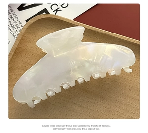 Detail of pearlescent white acetate hair claw clip on a wooden tray with soft lighting