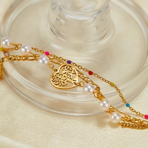 Detail of gold multilayer bracelet featuring a heart pendant, pearls, and colorful beads