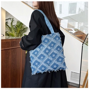 Blue denim tote bag with star patch and frayed edges shown in a lifestyle model shot