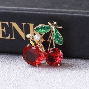 Detailed close-up of cherry brooch with red zircon stones, green leaves and a small bee