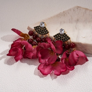Detail of red fabric petal earrings with gold base, black beads and clear diamonds
