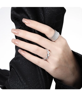 Detail of a textured wide silver band and a wavy diamond ring on fingers over black fabric