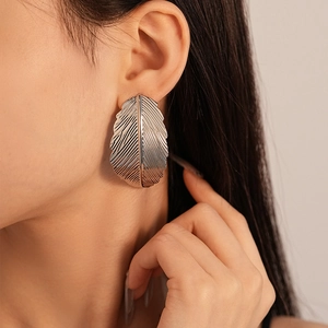 Macro shot of silver metal leaf earrings with intricate vein textures on model