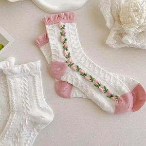Detail einer weißen Stricksocke mit rosa Tulpenstickerei und modischem Rüschenbündchen