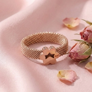 Close-up of rose gold mesh ring with cutout star and clover patterns on pink silk