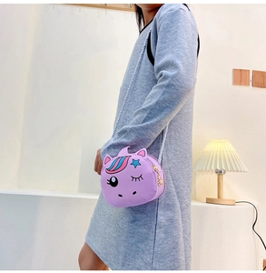 Girl wearing a purple unicorn crossbody bag with a white woven strap in a cozy room