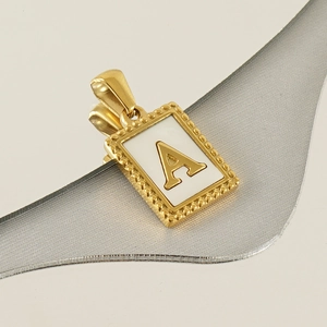 Detail eines goldenen Anhängers mit Buchstabe A und weißer Einlage auf Spiegelgrund