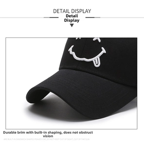 Close-up of a black baseball cap with white embroidered smiling face and curved brim