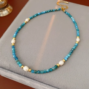 Detail of blue bead and pearl necklace with gold-plated clasp on a jewelry stand