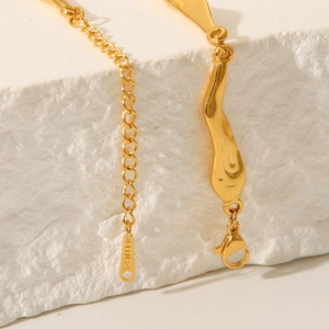 Close-up of golden irregular stainless steel pendant necklace on white textured stone