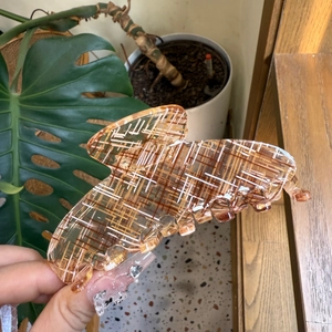 Detail shot of large amber acetate hair claw clip with stylish checkered pattern held in hand