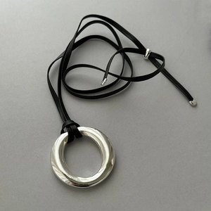 Close-up of a silver-toned minimalist ring pendant on a black leather cord necklace