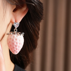 Detailed view of strawberry earrings with silver leaf and heart-shaped diamond on a model