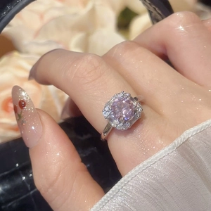 Close-up of a silver ring with round purple gemstone and diamond halo on finger
