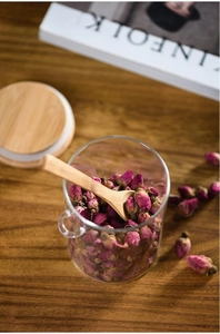 Detail of clear glass jar with dried roses, wooden spoon, and lid on a rustic table