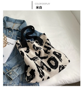 Detail of cream knitted tote bag with black graffiti patterns on a denim jacket