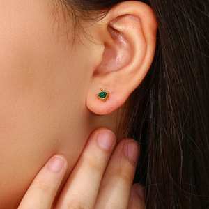 Close-up of minimalist gold earring with green round gemstone worn by a model