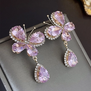 Gros plan de boucles d'oreilles papillon dorées avec pierres violettes et cristaux blancs
