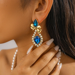 Detail of vintage gold bow earrings with blue gemstone and sparkling rhinestones