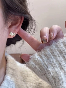 Close-up of gold plated puppy earrings with pavé zircons worn by a model in warm light