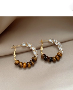 Detailed shot of gold hoop earrings with sparkling zircons and tiger eye beads
