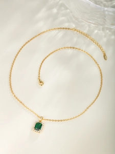 Detail shot of a vintage gold necklace featuring a square green gemstone pendant with small diamonds