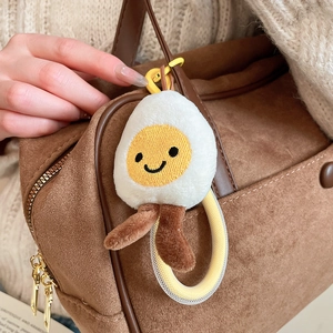 Close-up of a cute poached egg plush keychain with smiling face on a brown suede bag