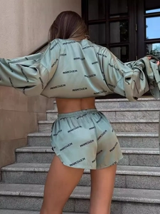 Green satin two-piece set with long sleeve crop top and shorts featuring logo prints