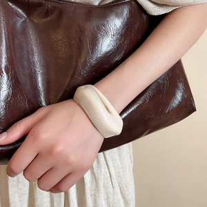 Close-up of cream acrylic bangle with irregular thick design worn on wrist