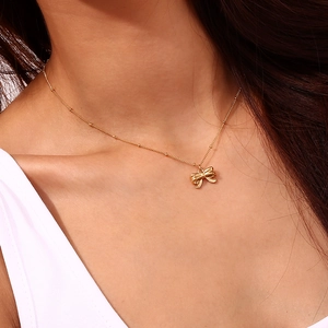 Detail of a minimalist gold bow pendant on a fine beaded chain worn by a female model