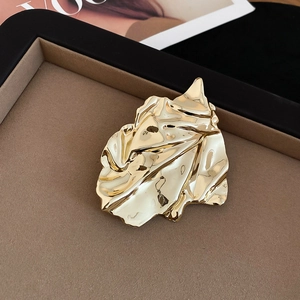 Macro shot of wrinkled gold leaf brooch with high-polish mirror finish on a velvet tray