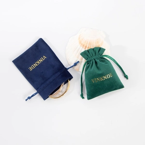Detail of velvet drawstring jewelry pouches in navy and emerald green with gold branding