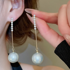 Detailed view of long tassel pearl earrings with sparkling diamonds and gold chain