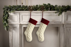 Close-up of white cable knit Christmas stockings hanging on a festive mantel with pine