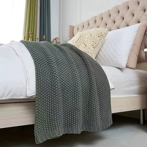 Chunky knit dark gray throw blanket with tassels in a cozy Nordic bedroom setting