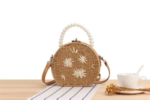 Détail d'un sac rond en paille avec fleurs tissées et poignée en perles sur table en bois