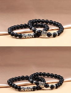 Detail of beaded bracelets featuring matte and glossy black stones with owl charm and silver tube
