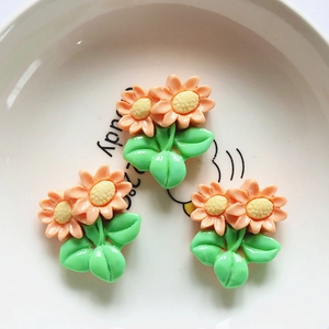 Detail shot of cute resin orange flower charms with green leaves on a white tray